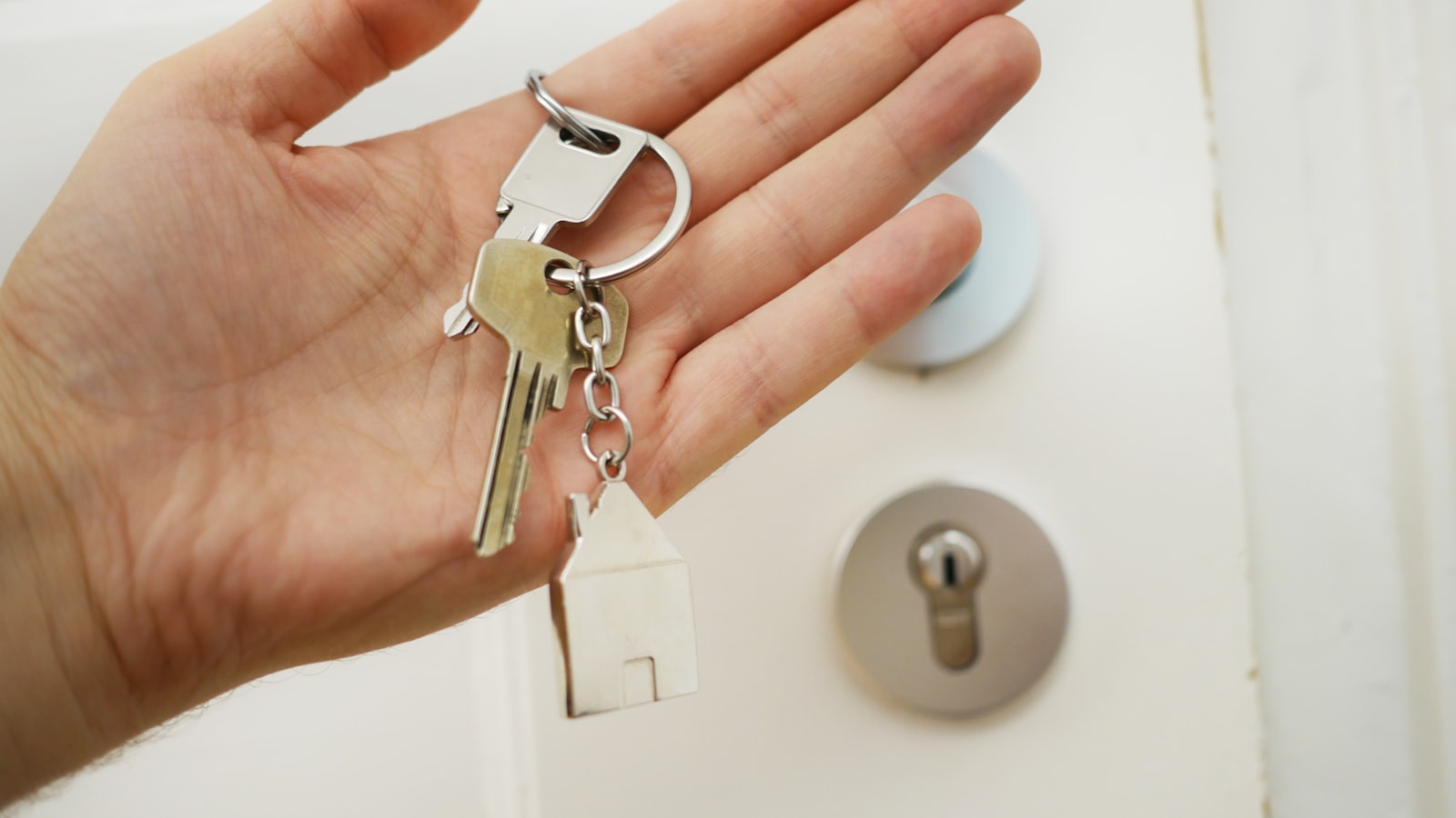 Main tenant un trousseau de clés avec un porte-clés en forme de maison devant une porte
